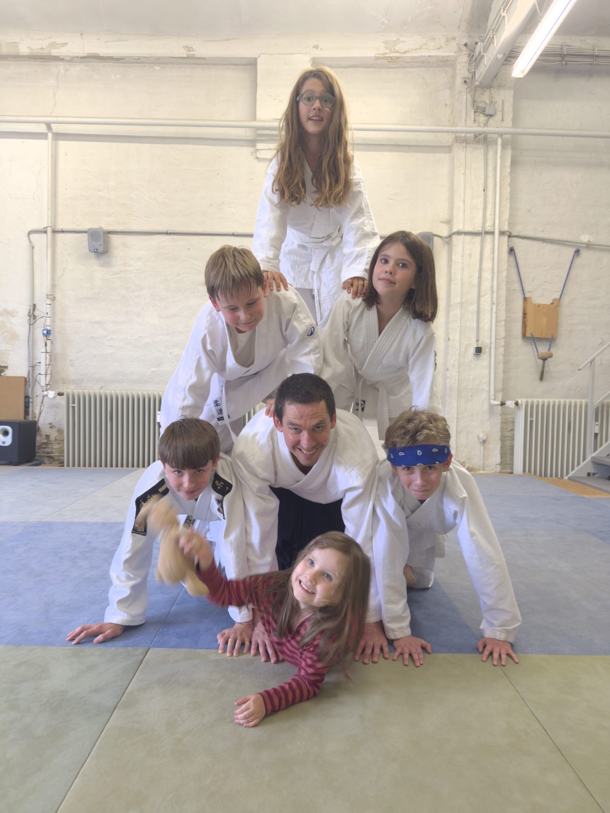 Kinder in weißen Aikido-Anzügen bilden mit Hoyu eine Menschenpyramide auf der Matte